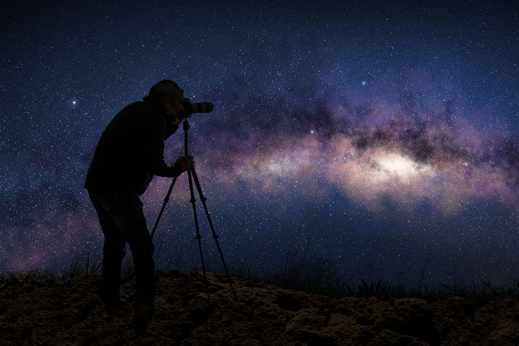 Silhouette of a photographer shooting the milky way in a starry night sky.